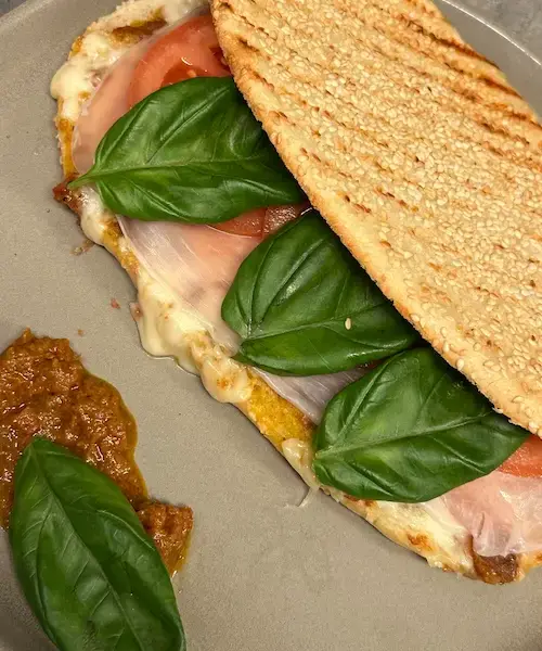 Knusprig angebratenes Panini Ciao Bella! mit rotem Pesto, Mozzarella, Tomaten, Serranoschinken und Basilikum