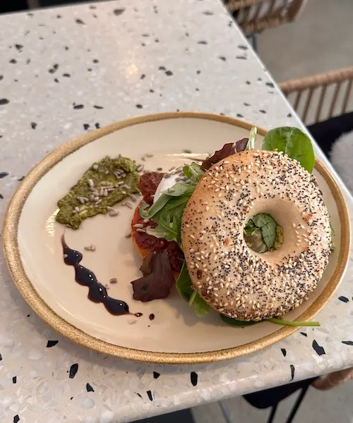 Tosca Bagel mit Burrata, getrockneten Tomaten, Wildkräutersalat, grünem Pesto und Sonnenblumenkernen